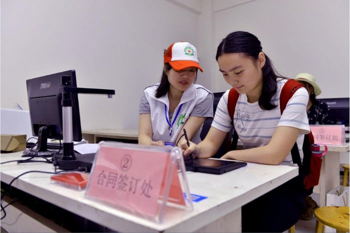 一名首贷大学新生在志愿者指导下在电子手写板上签字确认。
